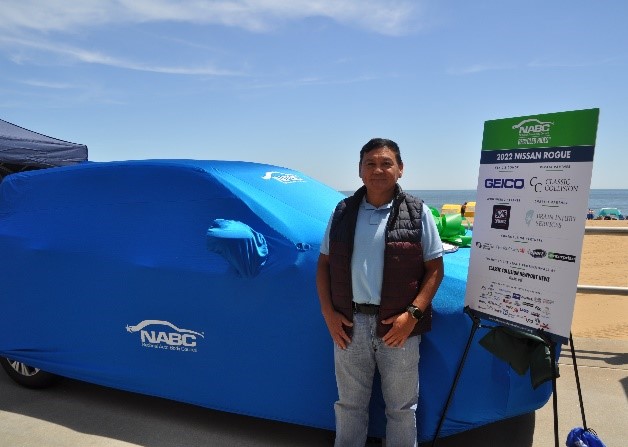 Victor Espinoza standing with his blanketed NABC Recycled Rides vehicle
